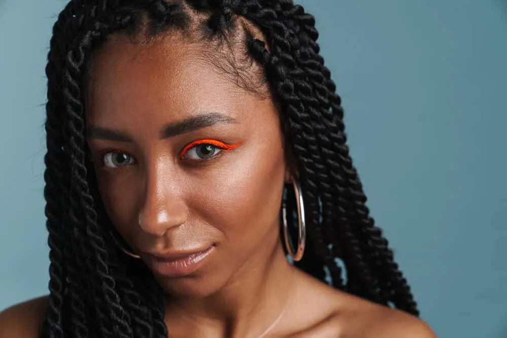 How To Clean Braided Hair Without Washing or Ruining Your Braids 2 Black woman with box braids and a stressed scalp wearing red eye shadow and silver hoop earrings.