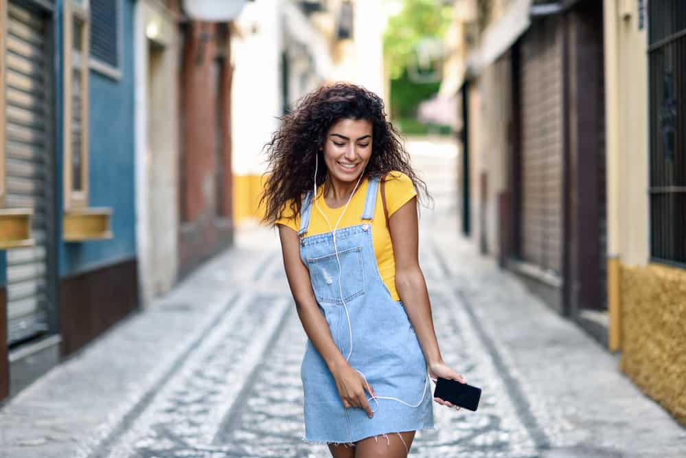 Cute young black girl with a wavy hair texture wearing an overall blue jean outfit and a casual t-shirt.