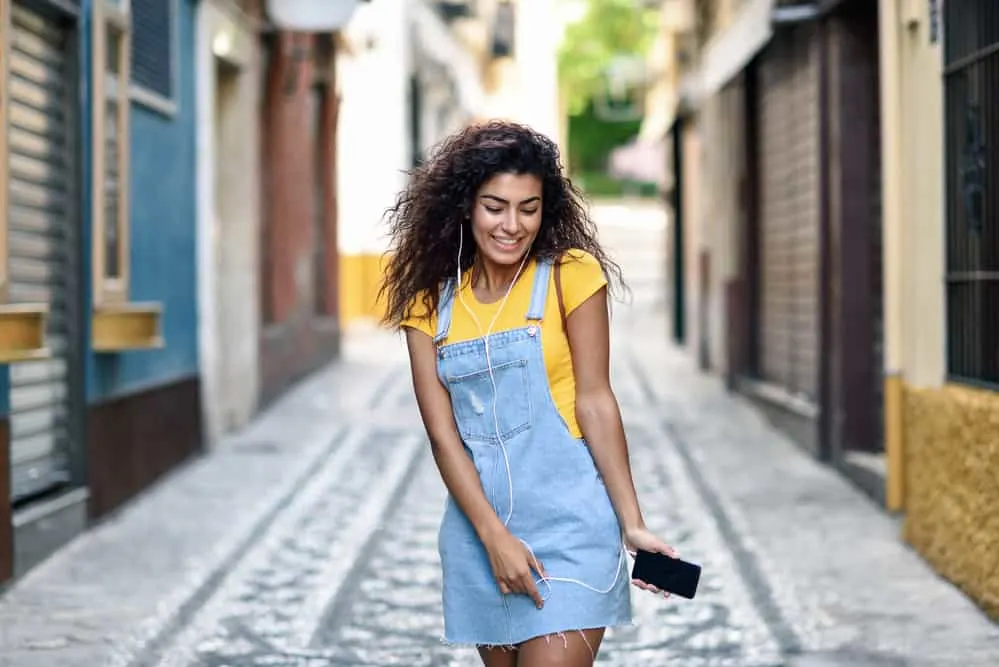 How to Get Waves With Straight Hair for Beginners: Step by Step 20 Cute young black girl with a wavy hair texture wearing an overall blue jean outfit and a casual t-shirt.