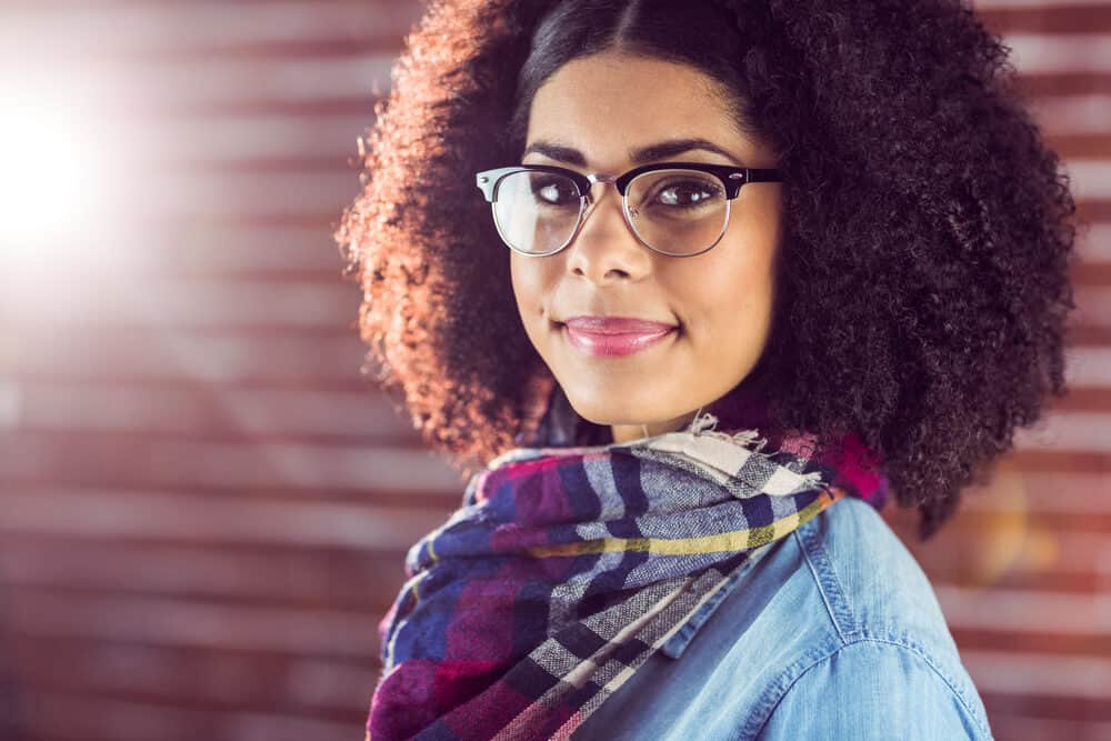African female wearing eyeglasses, red lipstick, and colorful scarf, and a blue jean shirt.