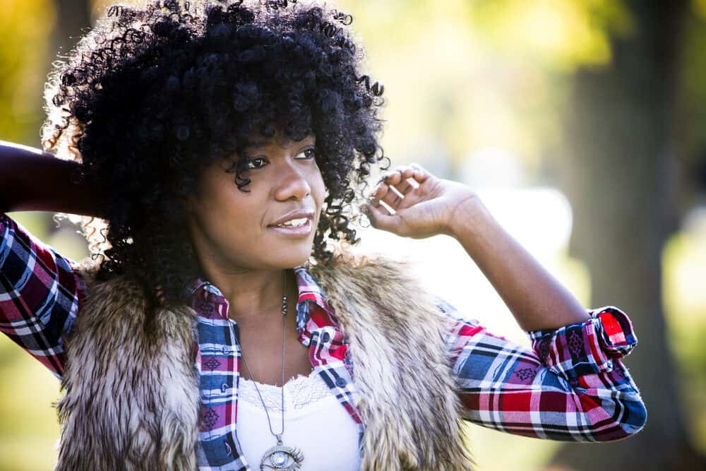 A young African woman with curly tresses is seen wearing a blue and red shirt and natural-looking cosmetics.