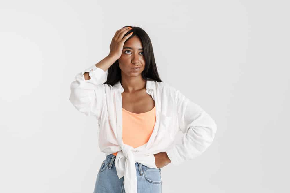 Young black girl with her hand on her own hair wearing an orange undershirt, white dress shirt, and blue jeans.