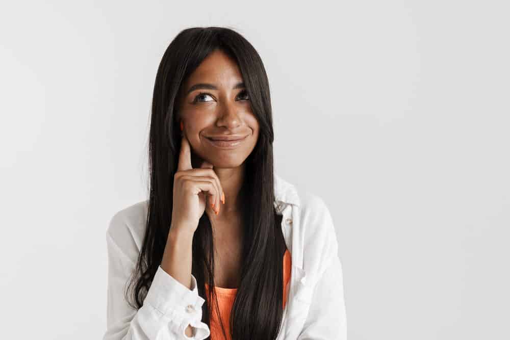 Black college student wearing a full lace wig with an orange t-shirt, white over-shirt, and orange fingernail polish.