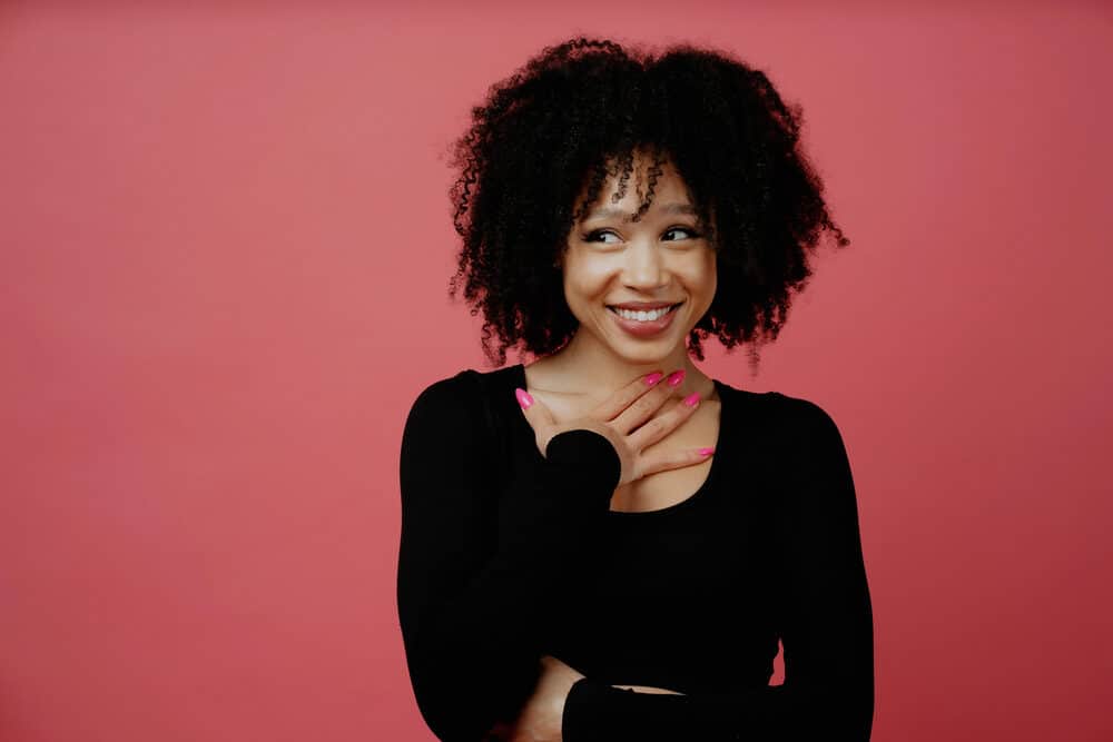 A black woman with curly hair follicles wearing a black shirt, red lipstick, and pink fingernails.