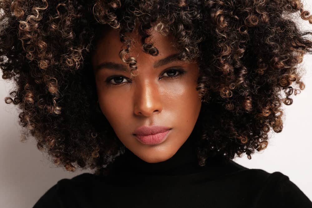 Attractive African American female with curly color-treated hair strands dyed with permanent dye.