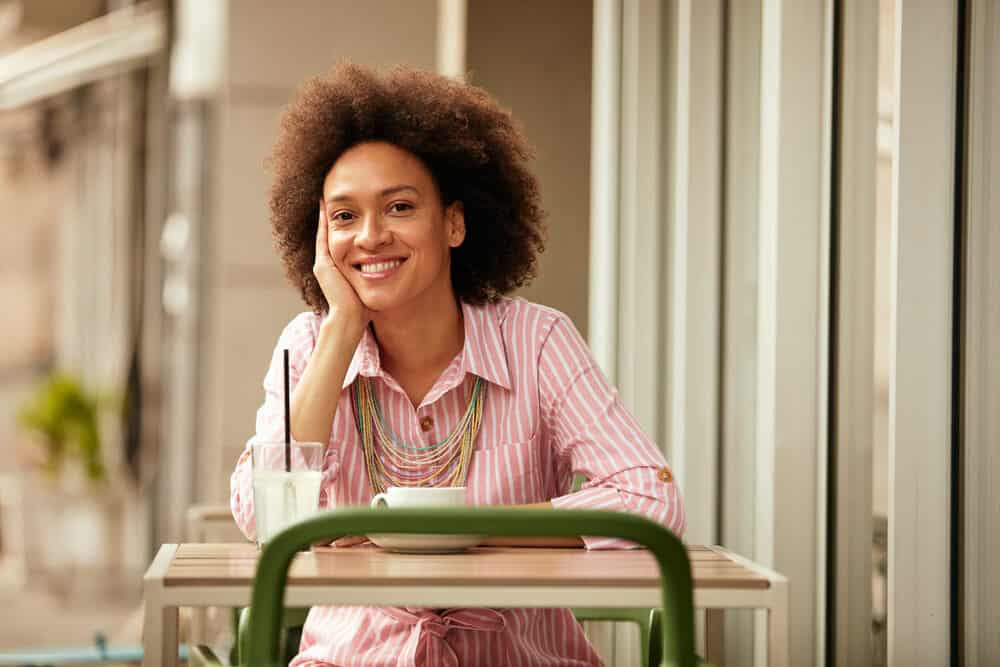 Cute girl having a cup of coffee with a medium skin tone wearing a wash and go hairdo on curly brown hair.