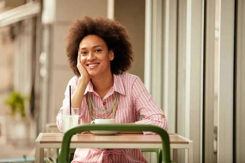 The 11 Best Unnatural Hair Colors for Cool Skin Tones 1 Cute girl having a cup of coffee with a medium skin tone wearing a wash and go hairdo on curly brown hair.