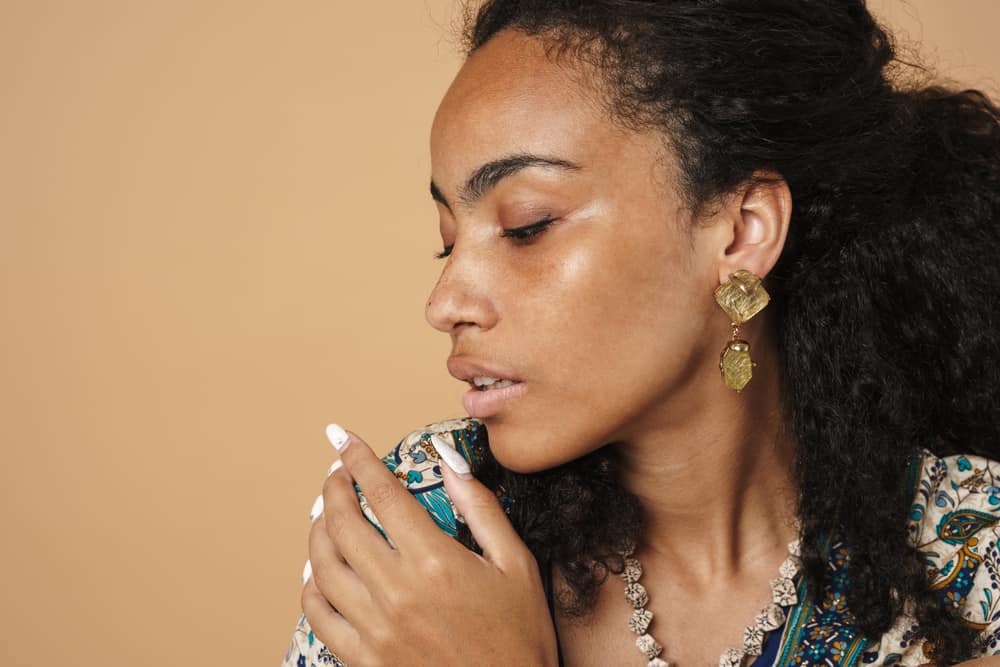 A light-skinned black lady with color-treated hair wearing beautiful gold jewelry and a colorful casual shirt.