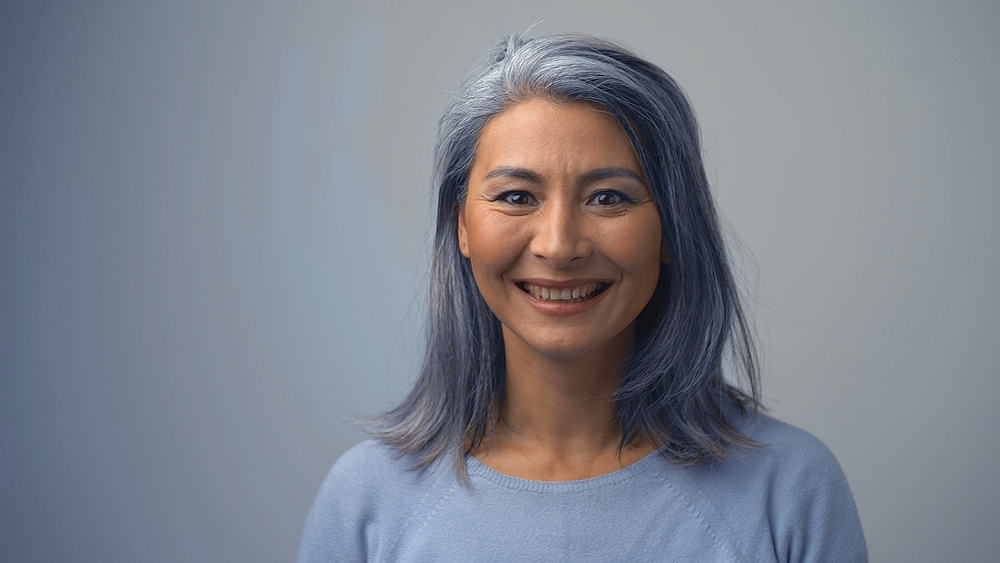 A charming Asian woman that's going through a gray hair transition after a few washes with purple shampoo.