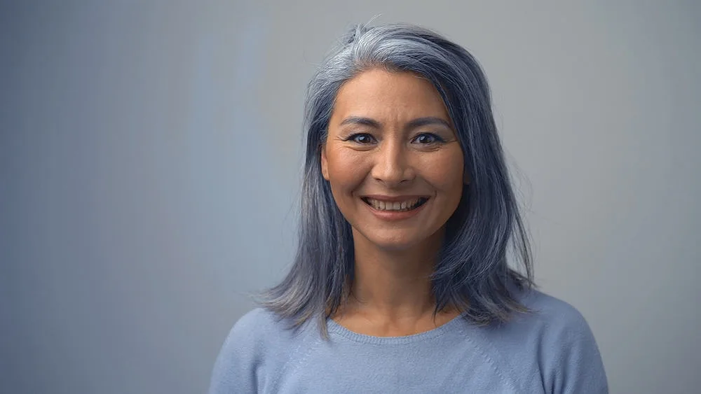 Removing Hair Color to Go Grey at Home: DIY How-to Guide 7 A charming Asian woman that's going through a gray hair transition after a few washes with purple shampoo.