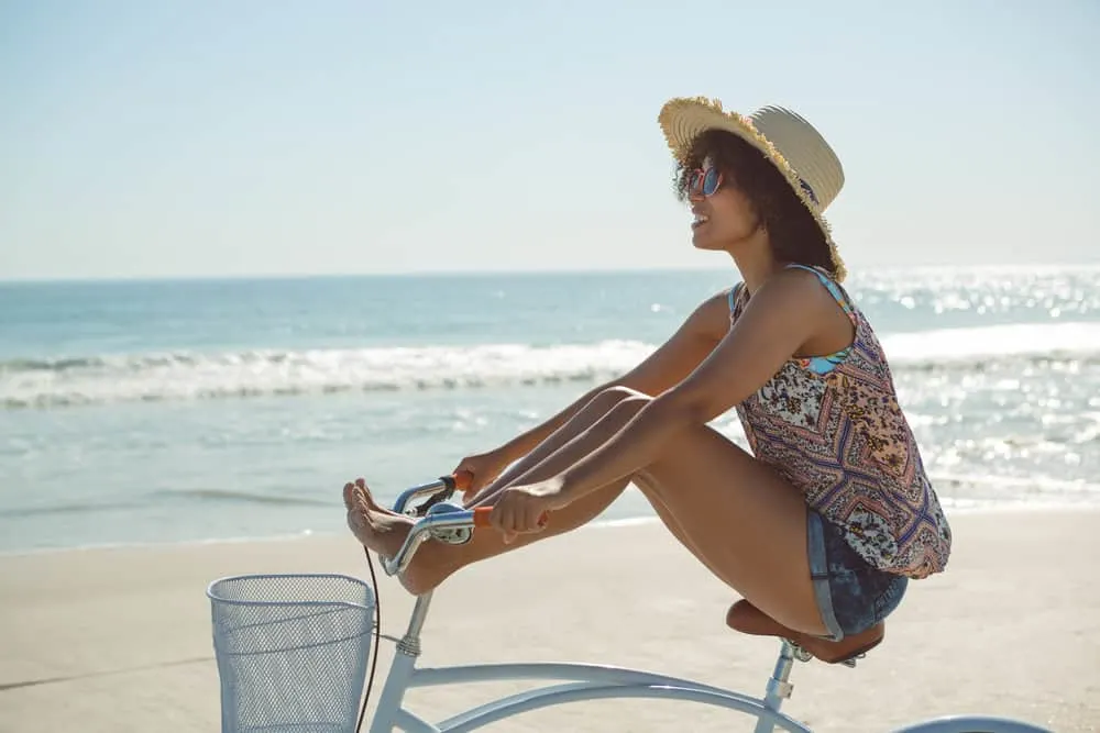 Why Is My Hair Curly When Wet? How to Stop Hair From Curling 8 Young black woman with wavy hair wearing casual summer clothes and a straw hat while riding a bike at the beach.