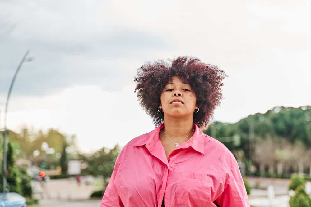 Black girl with a light brown natural color on fine hair with kinky curls covering her whole head.