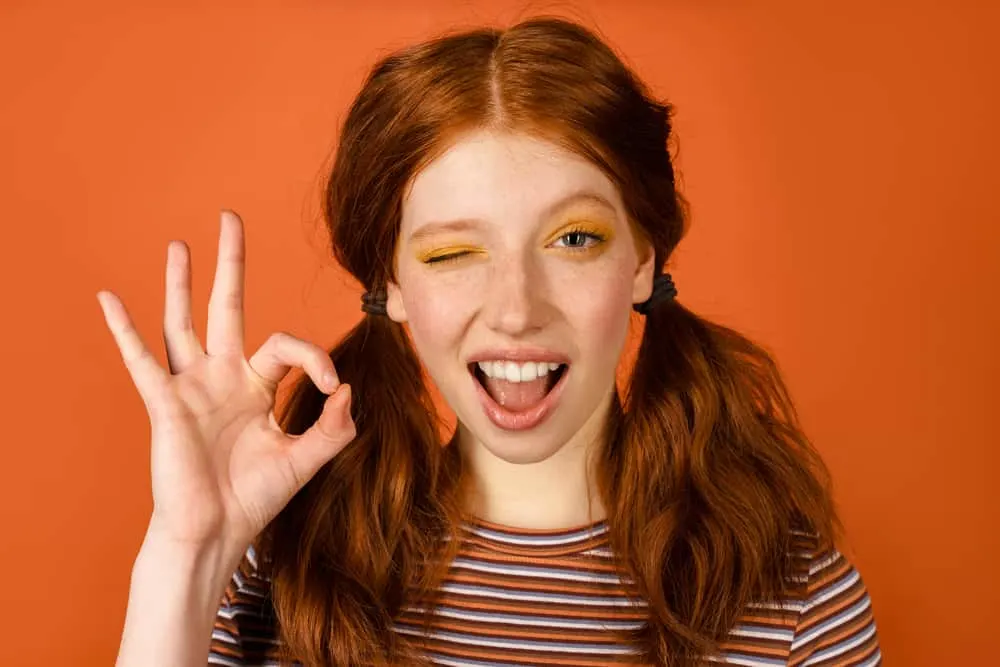How to Fix Orange Hair With Box Dye: DIY Step-By-Step Guide 11 A white girl with pigtails wearing her hair orange and pink lipstick while winking.