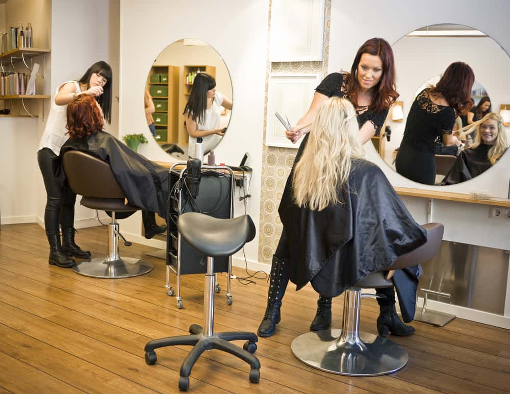 Two barbers hairstyling their clients in signature-style salons. 