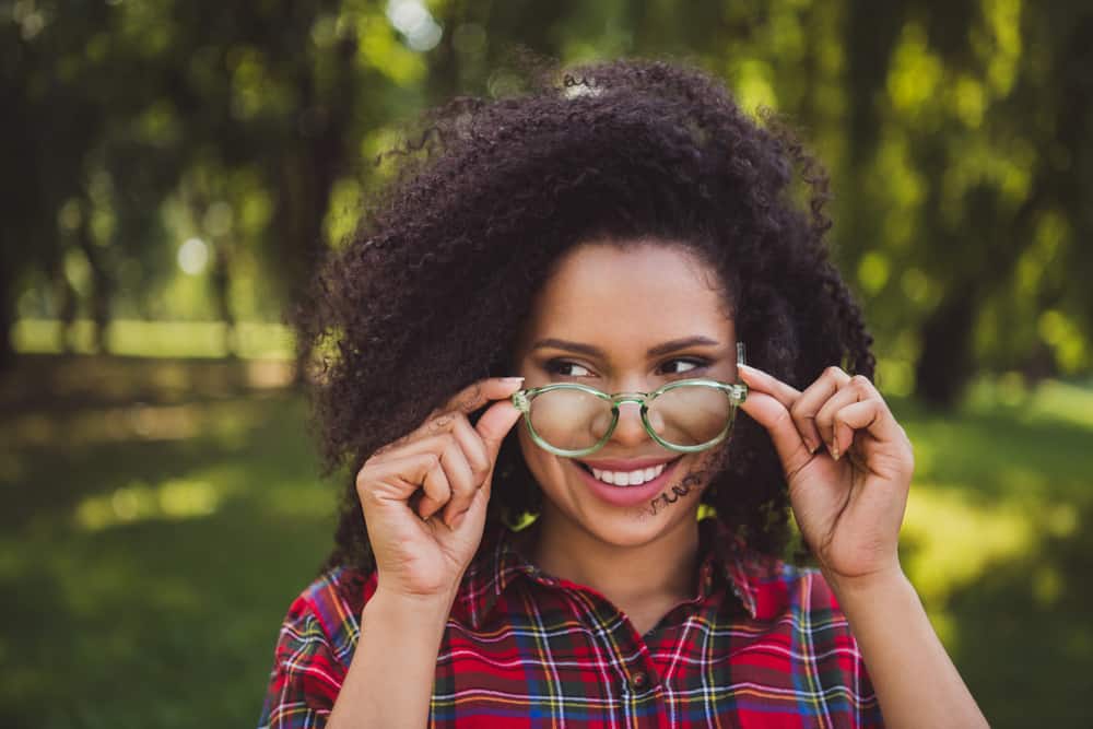 Young black female with layered curly hair wearing green eyeglasses from Warby Parker and a casual plaid shirt.