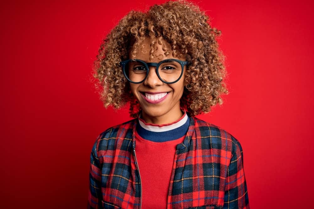 Cute black girl with chemically treated bleached hair follicles wearing a plaid jacket and black glasses.