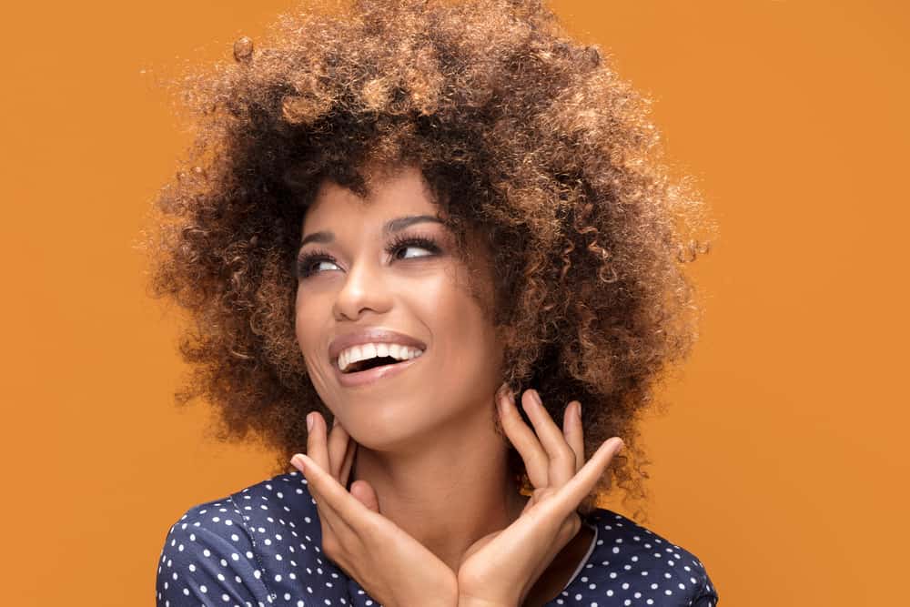 Light-skinned black woman with a dark brown, vibrant natural hair color wearing blonde colored hair.