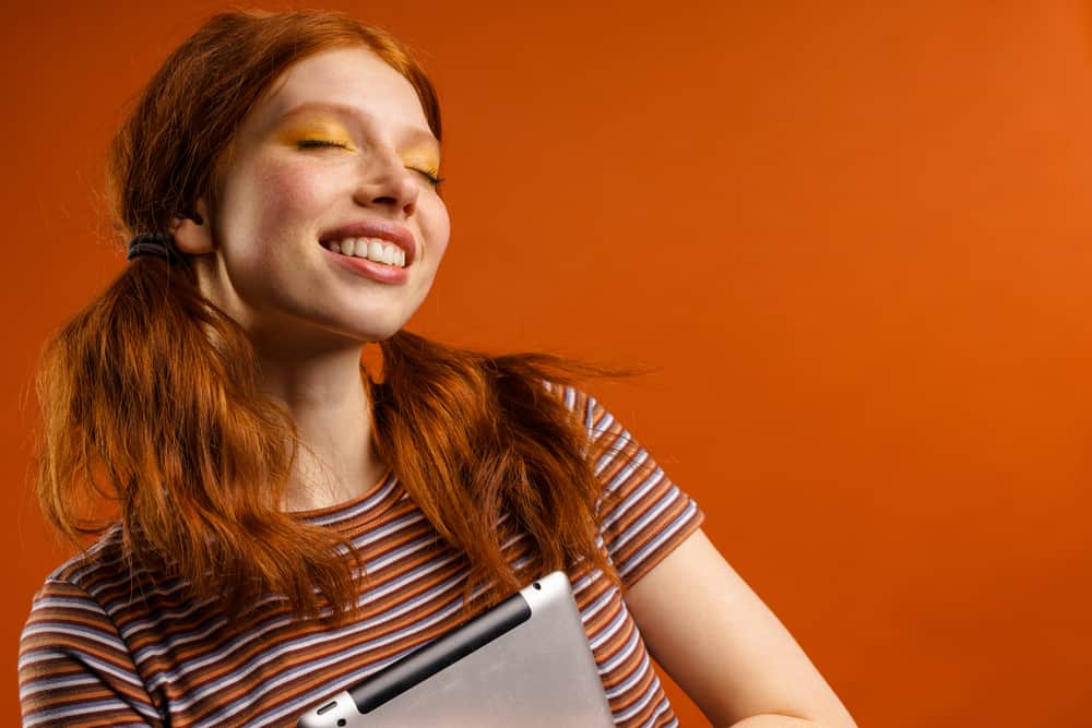 Female holding an Apple iPad with dark orange after using a blue toning shampoo and purple toner.