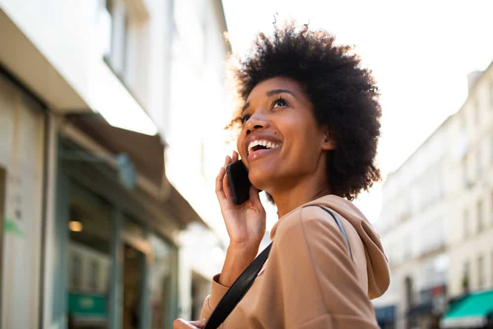 A lady walking down the street talking on a mobile phone with long curly hair styled with Moroccan argan oil.