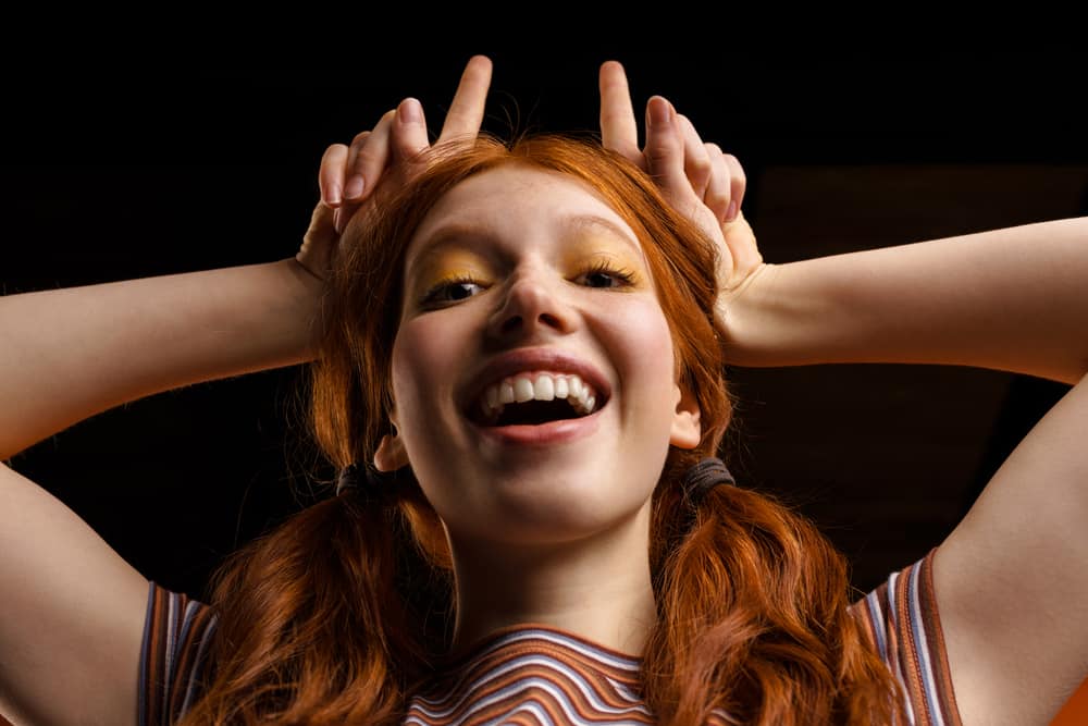 Young ginger, female, after hair dye made her hair turn orange pointing upward with her fingers.