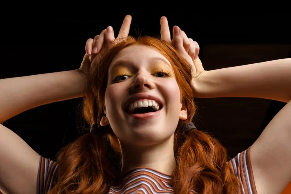 How to Fix Orange Hair With Box Dye: DIY Step-By-Step Guide 19 Young ginger, female, after hair dye made her hair turn orange pointing upward with her fingers.