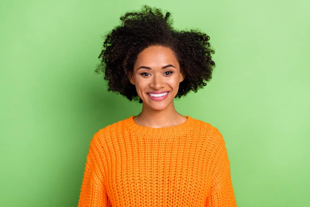 Optimistic black lady without any noticeable facial hair wearing a casual orange sweater on a chilly winter day.