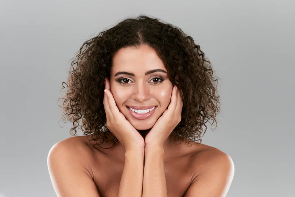 A female with mid-length oily hair from argan oil is holding her hands under her chin.