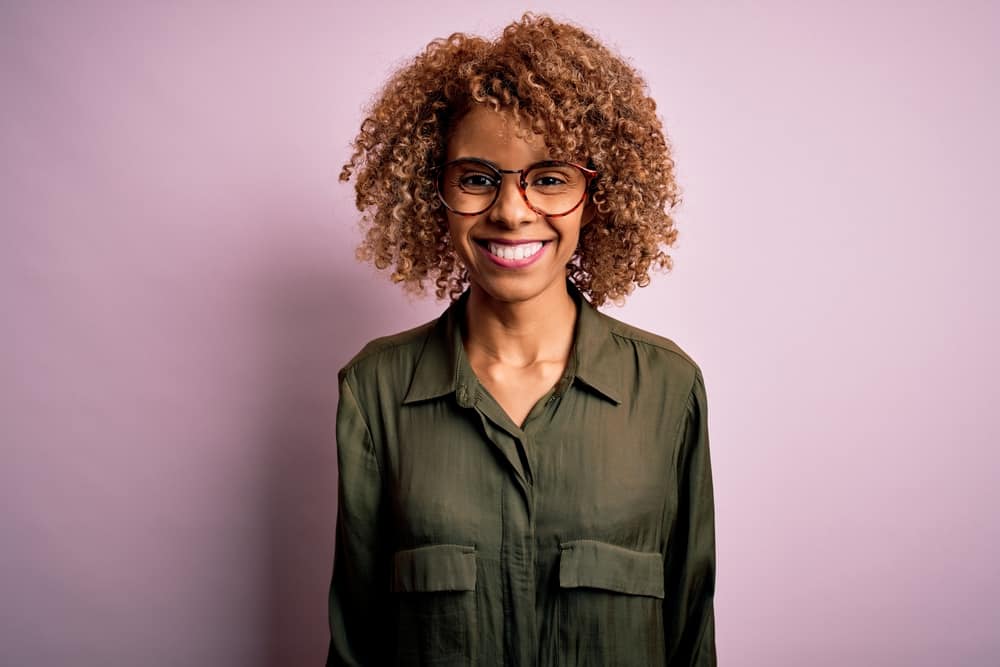 A happy black woman that's smiling because Adore smells good after using it within her hair routine.