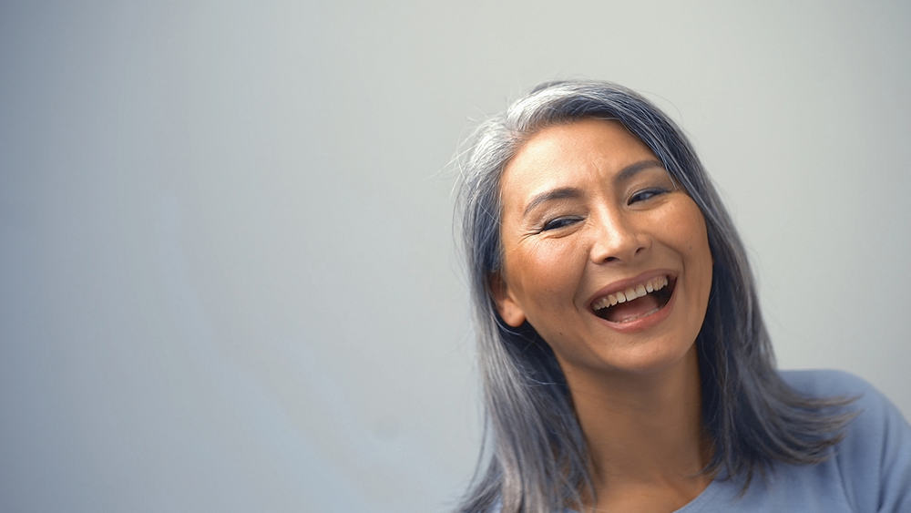 Senior Asian female with darker hair enjoying a good laugh while wearing casual clothes.