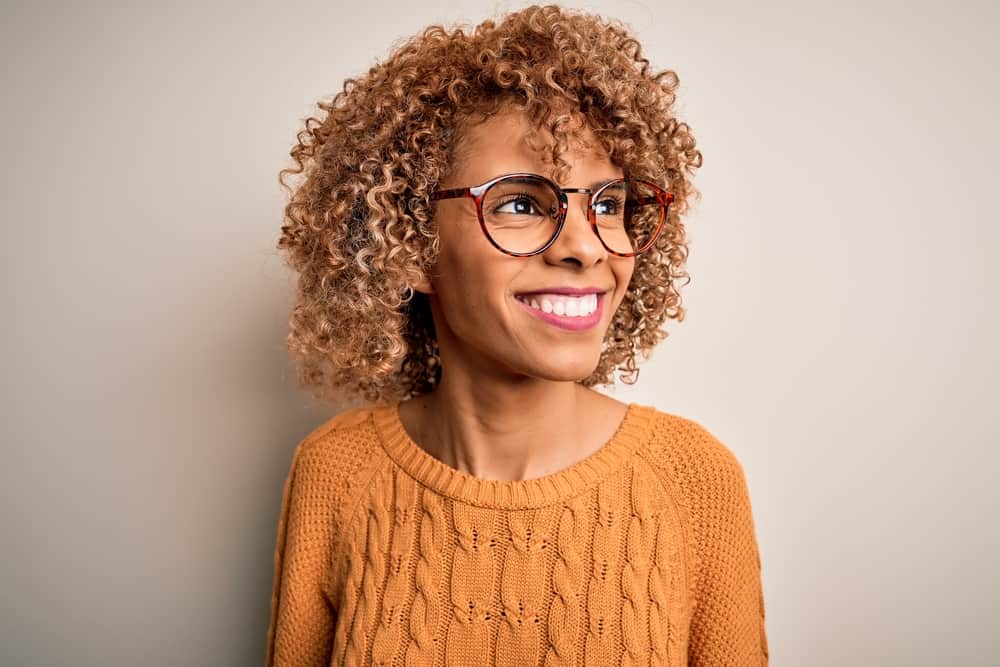 A black girl with a brown semi-permanent hair dye on her natural curls wearing a natural yuzu cranberry fragrance.