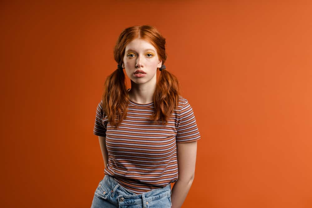 Cute young ginger woman with a brassy orange hair color wearing a casual shirt that's red, orange, and brown.