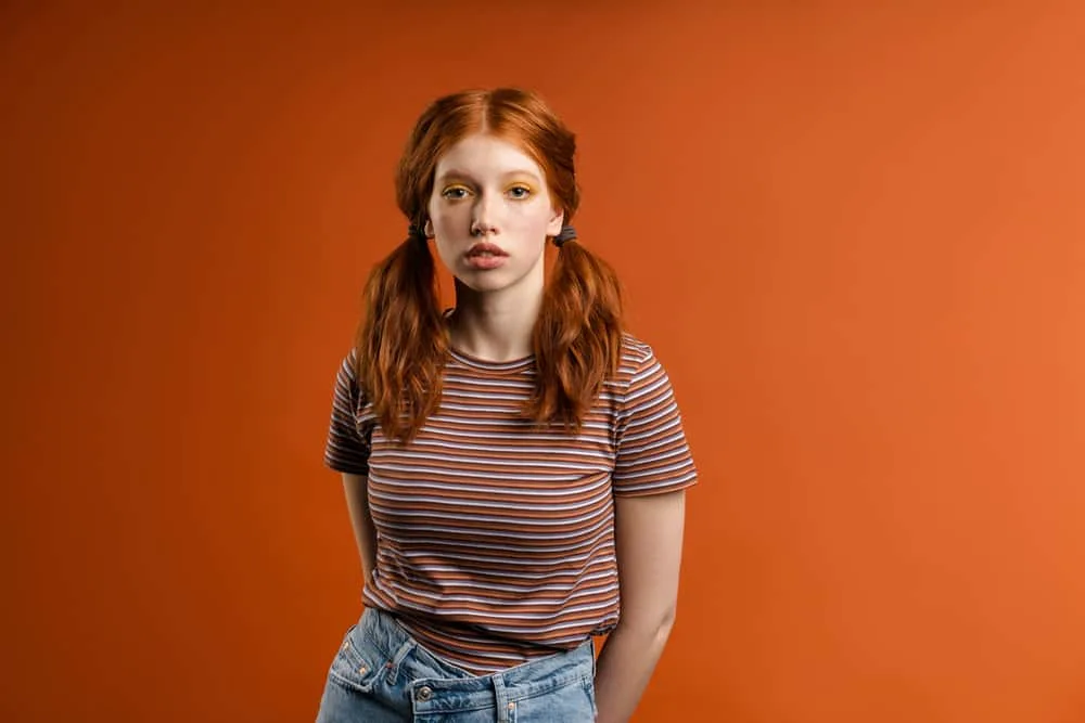 How to Fix Orange Hair With Box Dye: DIY Step-By-Step Guide 4 Cute young ginger woman with a brassy orange hair color wearing a casual shirt that's red, orange, and brown.