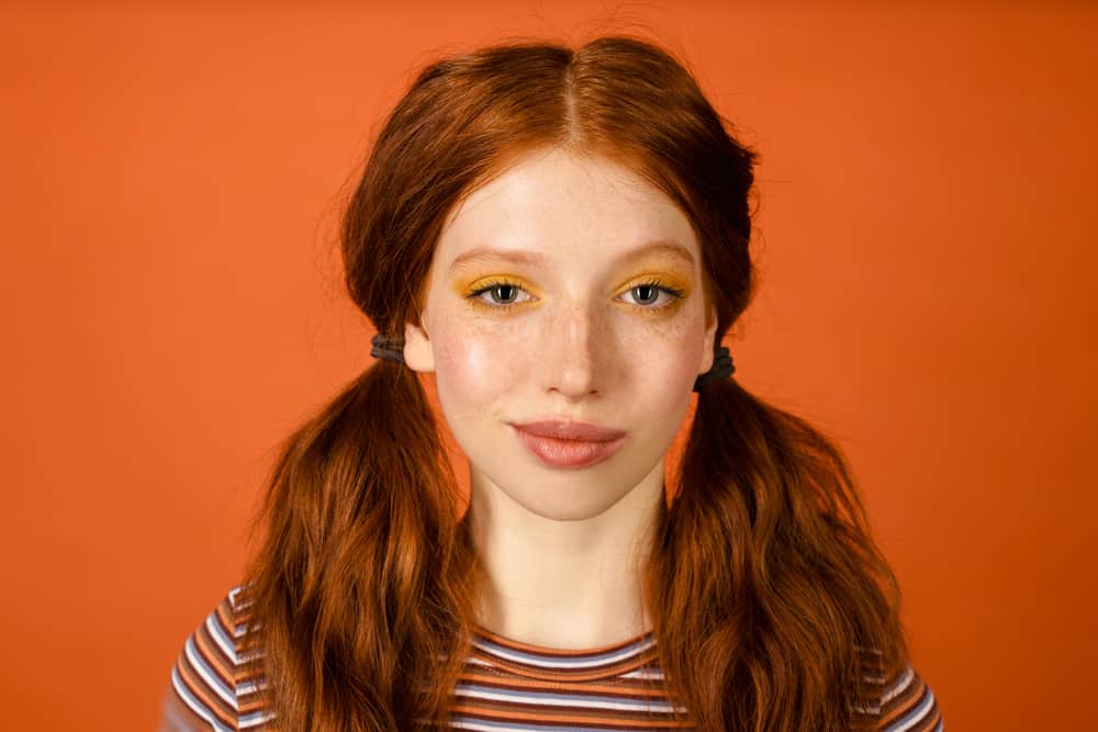 Cute female with 2A straight brassy hair with orange tones wearing her dark hair in a pigtail hairstyle.