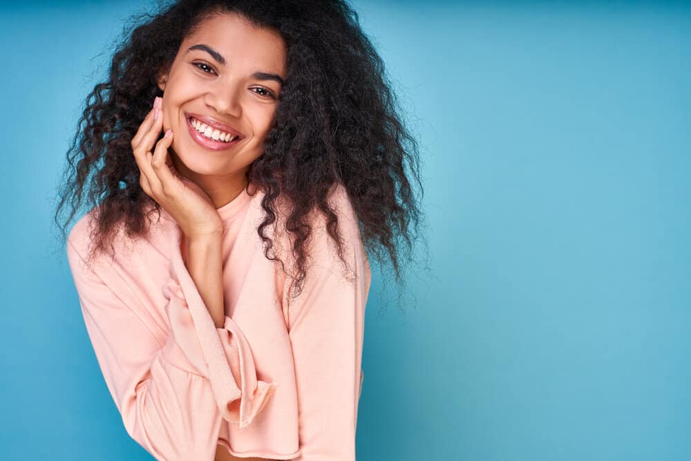 A joyful young African American lady with loose waves after using a leave-in conditioner to co-wash her waves.