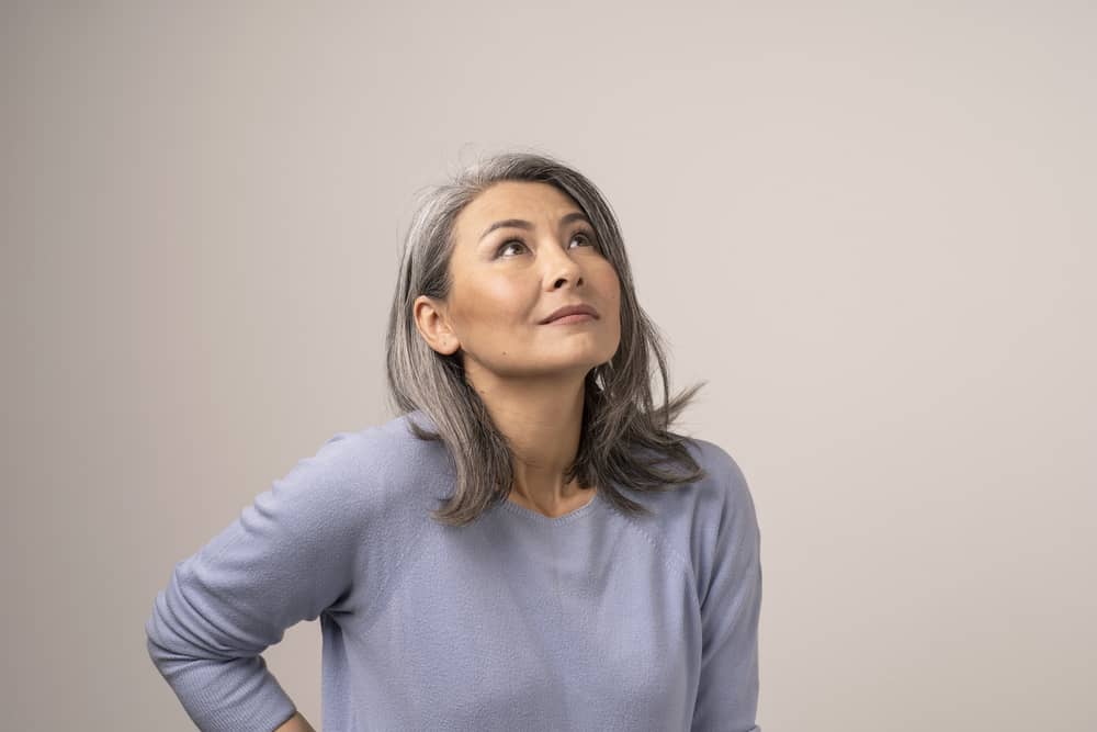 An older with natural hair looks upward while wearing a casual outfit and natural-looking makeup.