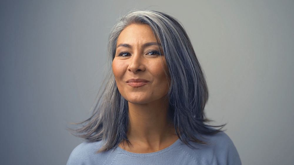 A lovely Asian woman with gray hair and olive-toned skin is letting her darker locks flow freely.