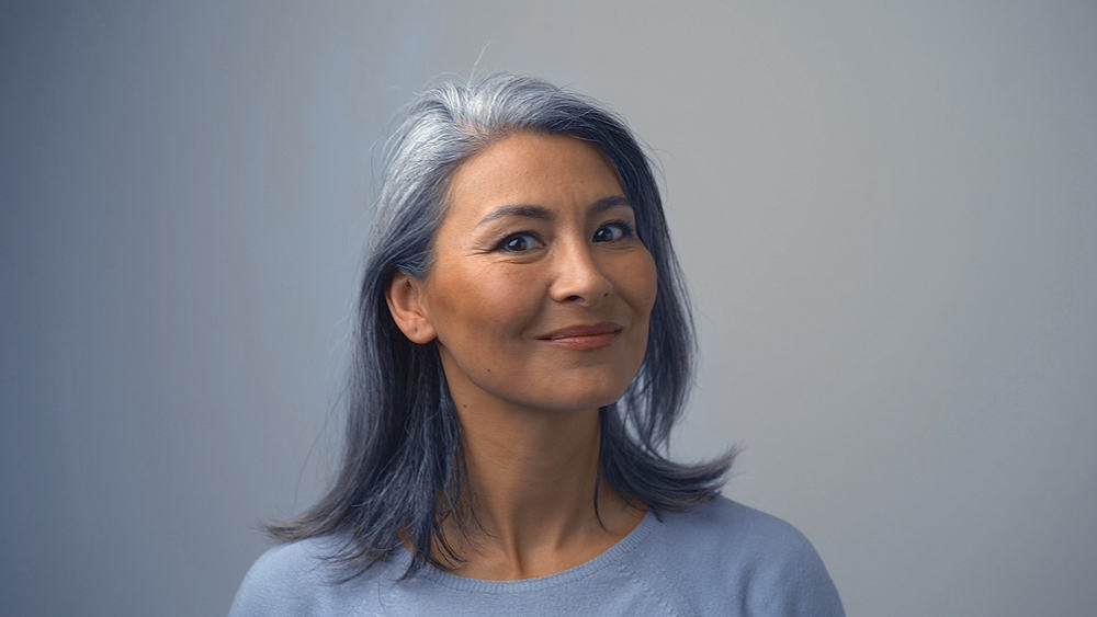 Beautiful mature woman with natural grey hair wearing a hat after removing permanent hair color.