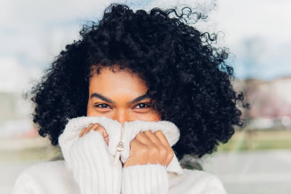 A young black lady wearing her colored hair dark in a curly afro hairstyle as she lets her natural roots grow.