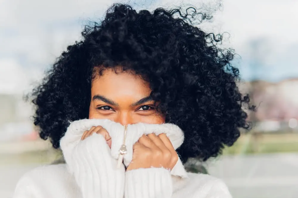 Does Dyeing Your Hair Black Damage It or Make It Healthier? 4 A young black lady wearing her colored hair dark in a curly afro hairstyle as she lets her natural roots grow.