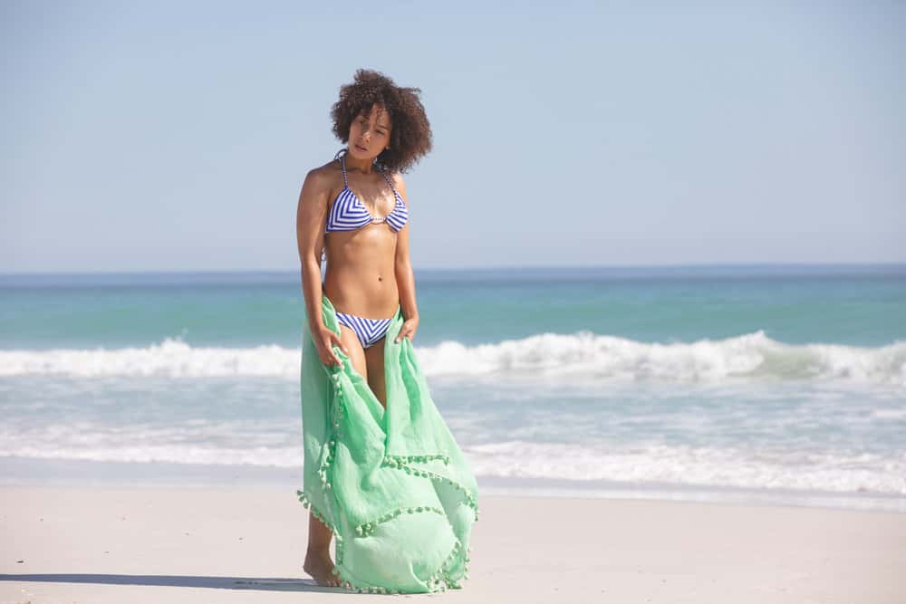 An adult female wearing a blue and white swimsuit after washing her wavy hair type in the ocean.