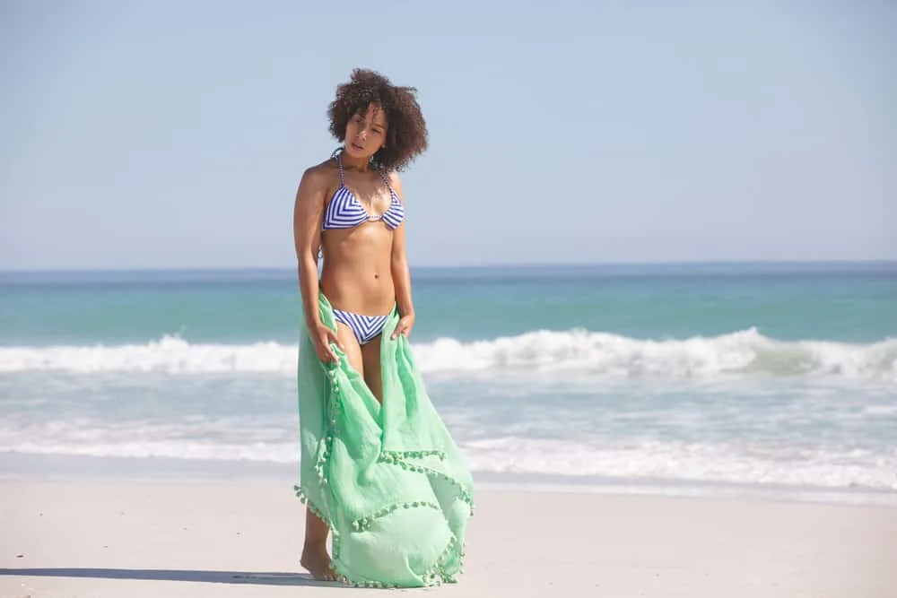 Why Is My Hair Curly When Wet? How to Stop Hair From Curling 5 An adult female wearing a blue and white swimsuit after washing her wavy hair type in the ocean.