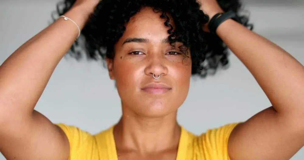 Cute black woman with frizzy hair capturing her curls in a pineapple hairstyle to preserve curls while sleeping. 