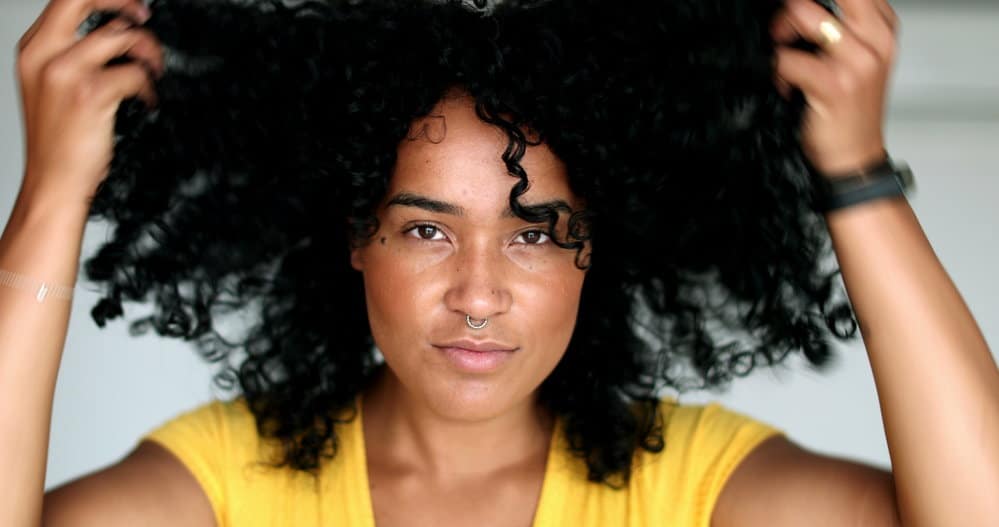 A young black woman with naturally curly hair gathered her loose hairs to keep her hair protected in a sleep bonnet.