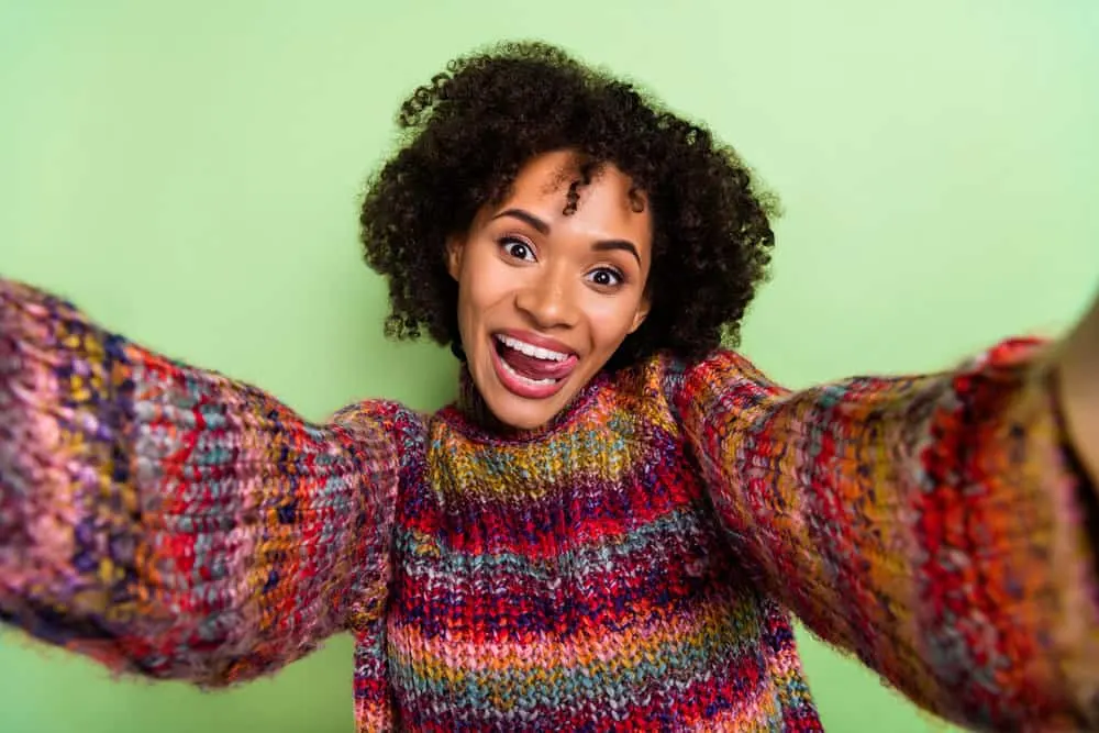 A positive young black woman with jet black hair wearing a fun, colorful holiday sweater.