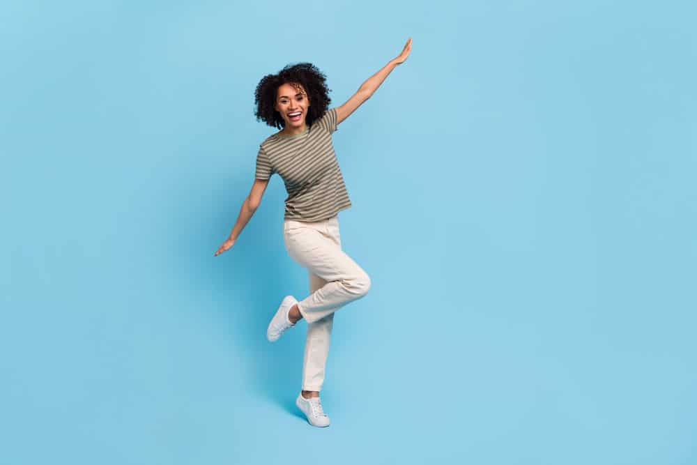 A lady with healthy hair wearing a green t-shirt and white jeans while dancing with friends.