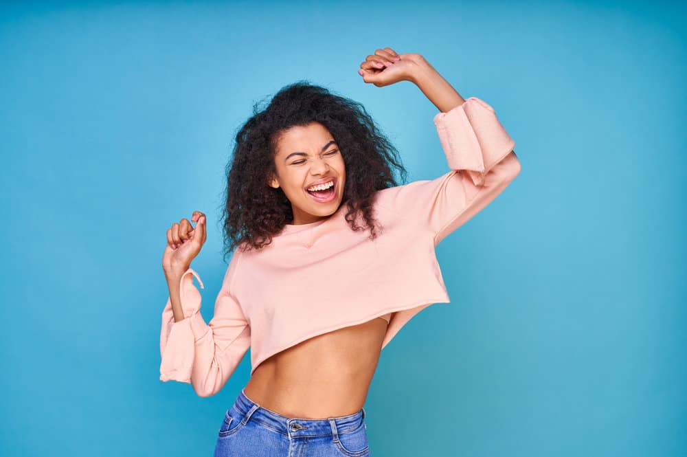 A positive dark-skinned black woman with wavy hair strands after using a sulfate-free shampoo on her curls. 