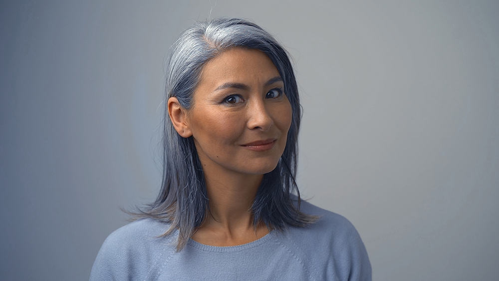 A gray-haired Asian woman in her fifties with permanent hair dye concealing her natural gray hair follicles.