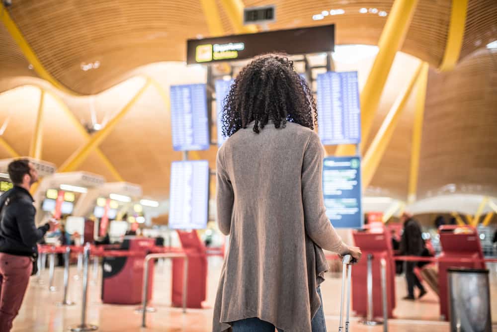 African American woman reviewing the flight information panel in the airport before going through airport security.