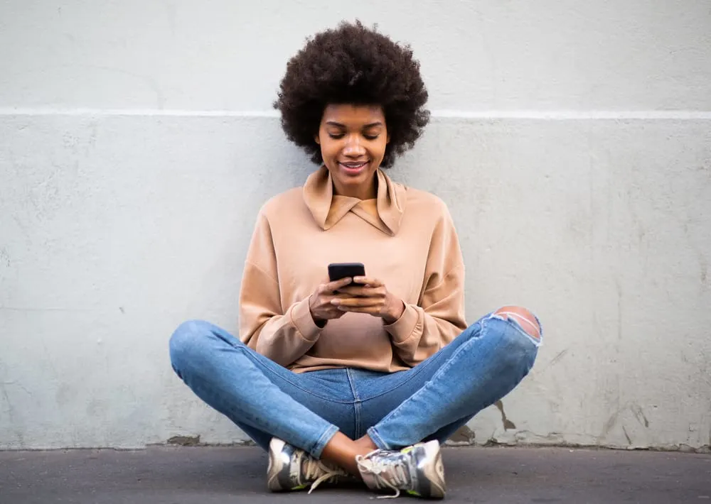 Why Is My Hair Matting Underneath? Prevent Hair From Matting 7 A black female wearing a casual shirt and jeans after air-drying her damp hair and using a moisturizing conditioner.