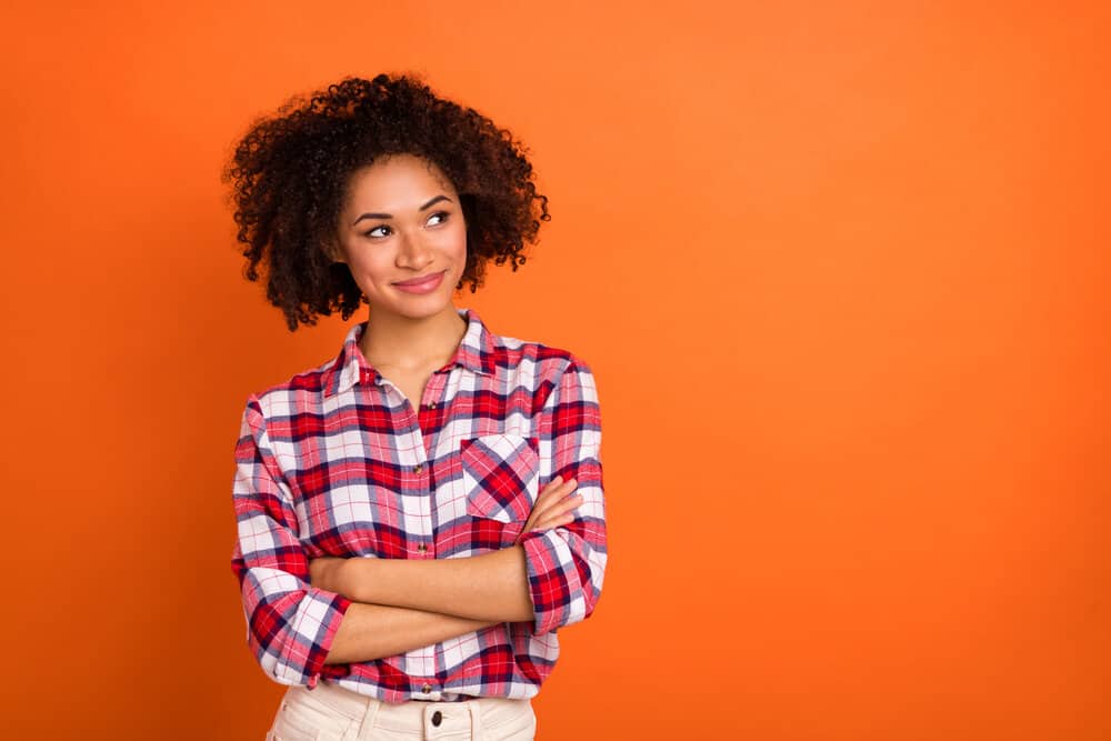 African American female with a dark brown eye color wearing a plaid shirt and beige jeans with kinky hair strands.